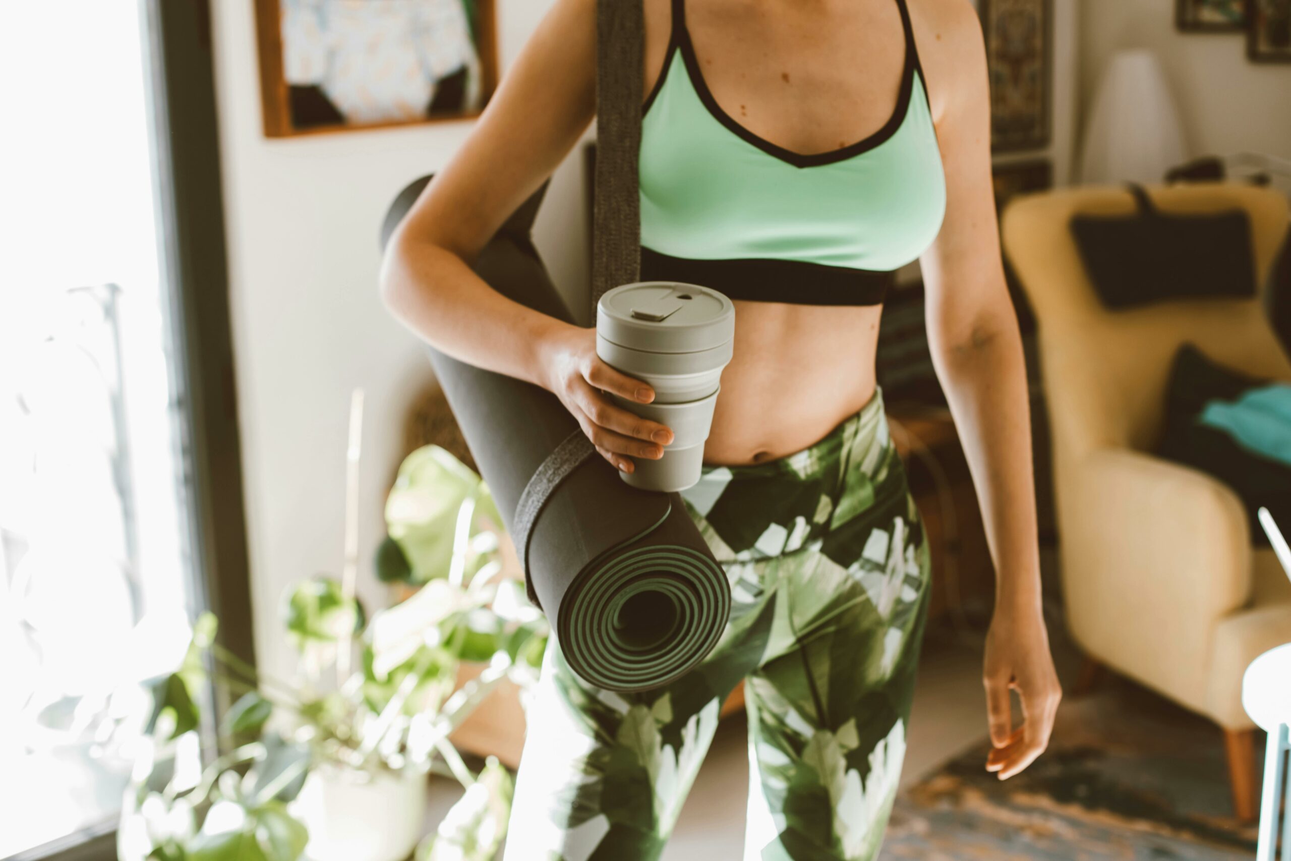 A woman arriving at a yoga class, holding a yoga mat and reusable coffee cup